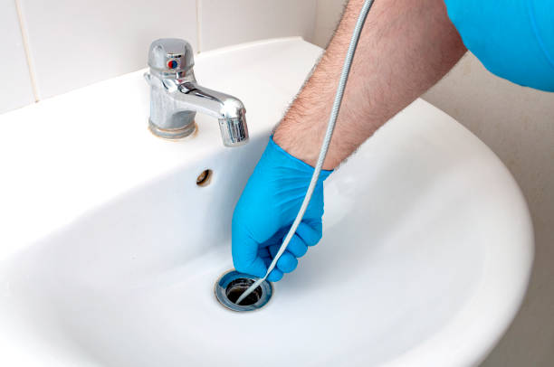 Hands in blue gloves performing drain cleaning in a residential sink.